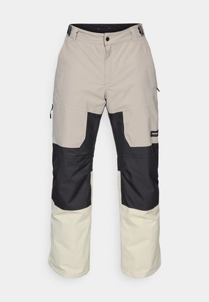 Beige og svarte snøvler med løs passform, som har kontrasterende paneler, glidelåslommer og en solid midje med knappelukke.