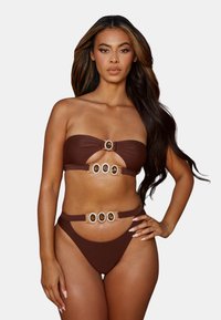 Ensemble bikini marron composé d'un haut bandeau sans bretelles avec une ouverture et des accents dorés. Le bas est taille haute avec des accessoires décoratifs. Texture lisse.