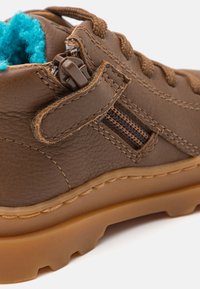 Brown leather boot with a textured finish, featuring a blue fleece lining, brown hardware, and a side zipper. Rubber sole with traction.