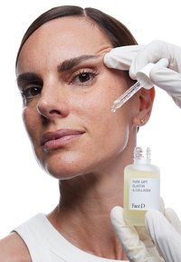 Flacone di siero per il viso con un liquido chiaro e texturizzato. Pipetta in vetro attaccata. Dettagli dell'etichetta: "PURE LIFT ELASTIN & COLLAGEN, FaceD." Modello che applica il siero.