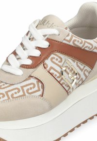 Baskets crème et marron présentant un motif texturé, des accents en cuir et en suède, des lacets blancs et un logo métallique sur le côté.