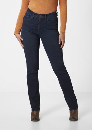 Dunkelblaue Skinny-Jeans mit hohem Bund, Vorderaschen und Knopfverschluss. Kombiniert mit einem eng anliegenden, orangefarbenen Langarmoberteil.