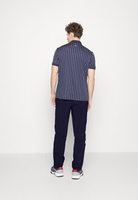 Marine gestreepte poloshirt met korte mouwen, gecombineerd met donkere broeken en grijze sneakers met rode accenten; ontworpen voor comfort en stijl.