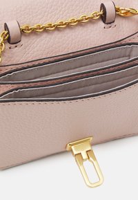 Piccola borsa a tracolla in pelle rosa con superficie testurizzata, tracolla in catena dorata e chiusura a scatto. L'interno presenta tre tasche organizzative.