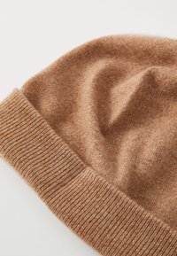 Chapeau en tricot marron avec un ourlet côtelé, texture douce et apparence confortable. Le tissu semble chaud et accueillant.