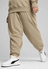 Vauhtipaidat beige väreissä, joissa on joustavat hihnat ja rento leikkaus, yhdistettyinä valkoisiin tennareihin, joissa on mustat yksityiskohdat. Pehmeä kangas on näkyvissä.