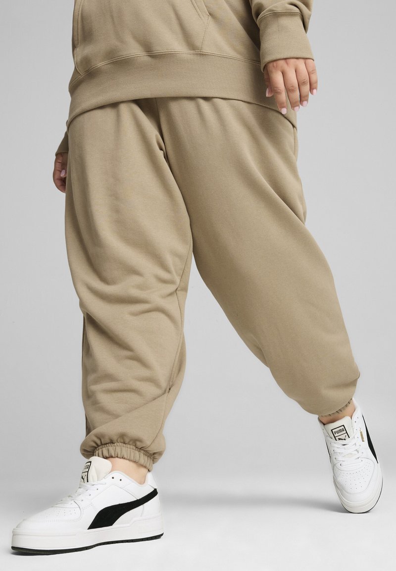 Vauhtipaidat beige väreissä, joissa on joustavat hihnat ja rento leikkaus, yhdistettyinä valkoisiin tennareihin, joissa on mustat yksityiskohdat. Pehmeä kangas on näkyvissä.