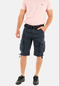 Marine cargobroek met meerdere zijzakken, trekkoord aan de onderkant en een losse fit, gecombineerd met een lichtroze T-shirt en zwarte sneakers.