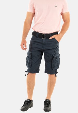 Marine cargobroek met meerdere zijzakken, trekkoord aan de onderkant en een losse fit, gecombineerd met een lichtroze T-shirt en zwarte sneakers.