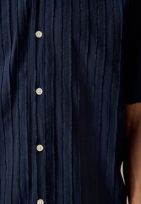 Marineblå skjorte med knapper og teksturerede, lodrette striber samt cremefarvede knapper. Har et blødt stof og et afslappet fit.