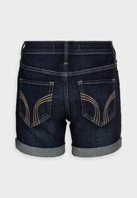 Shorts de mezclilla con un lavado oscuro, dobladillo enrollado, costuras detalladas en los bolsillos traseros y un diseño de cintura alta. Vista trasera mostrada.