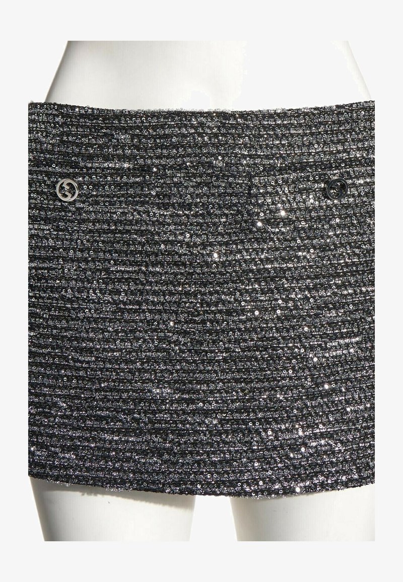 Mini-jupe noire texturée avec côtes horizontales et petites paillettes brillantes, avec deux boutons métalliques ronds près de la taille.