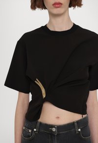 Melnā cropped T-kreklā ar savītu priekšpusi, kurai ir zelta izšuvums. Apvienots ar augsto jostasvietu tumšajiem džinsiem.