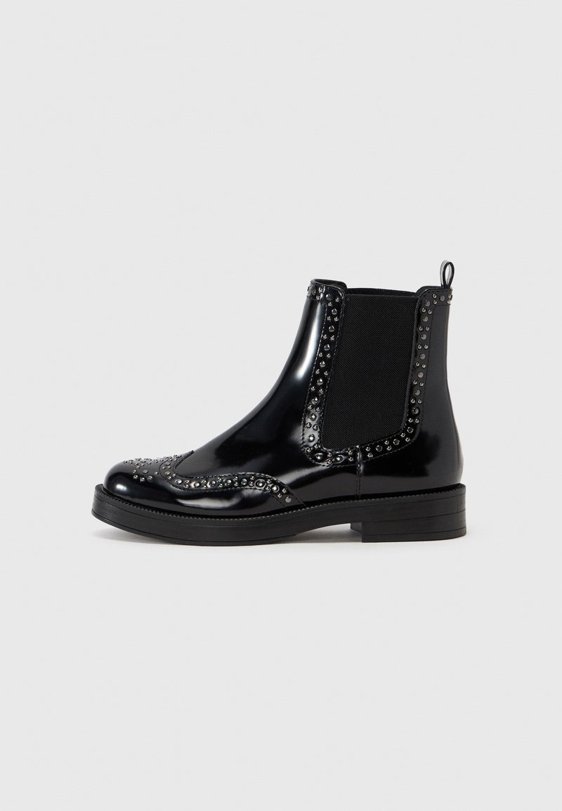 Bottine en cuir noir brillant avec détails brogue, petits clous le long des bords, empiècements latéraux élastiques et talon bas empilé.