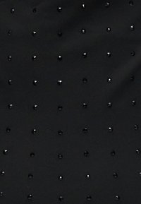 Μαύρο ύφασμα με ομοιόμορφα κατανεμημένα μικρά μαύρα γυαλιστερά καρφιά διατεταγμένα σε μοτίβο πλέγματος, δημιουργώντας μια υφή στην επιφάνεια.