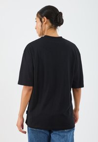 Svart oversized t-skjorte med korte ermer, laget av mykt stoff. Har rund hals og rett kant, brukt sammen med blå denimjeans.