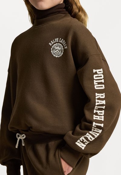 Sweatshirt castanho com gola alta, tecido texturizado e logótipo no peito e na manga. Realçado com um cordão cinza na cintura.