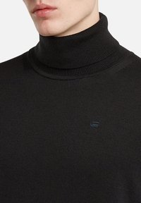 Schwarzer Rollkragenpullover mit gerippter Strickstruktur und einem kleinen, eingeprägten Logo auf der Brust. Hergestellt aus einem weichen, elastischen Stoff.