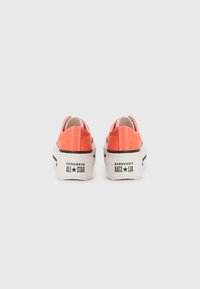 Orange canvas sneakers with white rubber sole, featuring black stripes and "Converse All Star" branding on the heel.