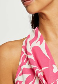 Top a halter multicolore rosa e bianco con un design drappeggiato e un tessuto morbido e leggero. Primo piano della spalla e del colletto.