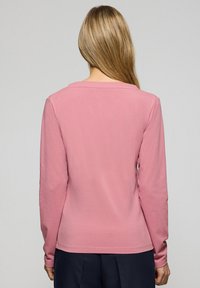 Långärmad rosa skjorta i mjukt tyg, med rak fåll och en enkel rund halsringning. Baksidan visar en slät, otexturerad yta.