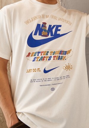 T-shirt blanc Nike avec texte coloré "A better tomorrow starts today,", le slogan "Just do it," et un graphique de pierres empilées au-dessus du logo.