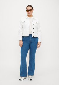 Chaqueta de mezclilla blanca, jeans acampanados azules y zapatillas. La chaqueta tiene dos bolsillos en el pecho y botones negros, con una textura de tela ligera.