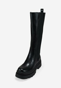 Bota alta de cuero negro con suela gruesa de tipo lug, panel lateral elástico y lengüeta, sobre un fondo blanco liso.
