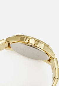 Reloj dorado con un acabado metálico suave, caja redonda, bisel detallado y corona texturizada. Presenta una pulsera de banda sólida.