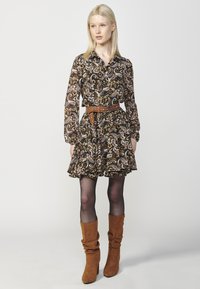 Zwart bloemenjurk met lange mouwen en paisleypatronen, met een taille die wordt benadrukt door een bruine riem, gelaagde gerimpelde rok, gecombineerd met bruine kniehoge laarzen.