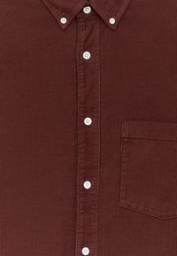 Burgunderfarbenes Cordhemd mit weißen Knöpfen, Button-Down-Kragen und einer Brusttasche auf der rechten Seite.