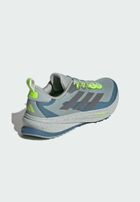 Keveysjuoksukenkä harmaana, sinisillä yksityiskohdilla, teksturoidulla verkkopäällä, kirkkailla vihreillä nauhoilla ja pilkullisella, kaarevalla pohjalla.