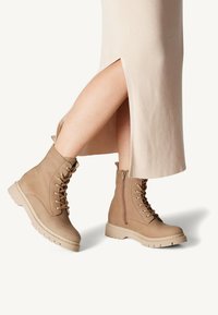 Tan lace-up boots with side zipper, featuring a textured leather upper, rubber sole, and thick heel, paired with a ribbed, beige midi dress.
