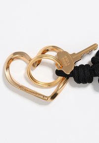 Portachiavi a forma di cuore in oro con due anelli, uno liscio e uno con finitura opaca, attaccato a una corda intrecciata nera, con una chiave.