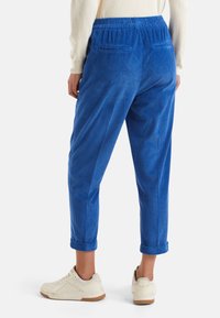 Pantalones de pana azul con un corte relajado, que cuentan con una cintura elástica, puños enrollados y dos bolsillos traseros. Combinados con zapatillas blancas.