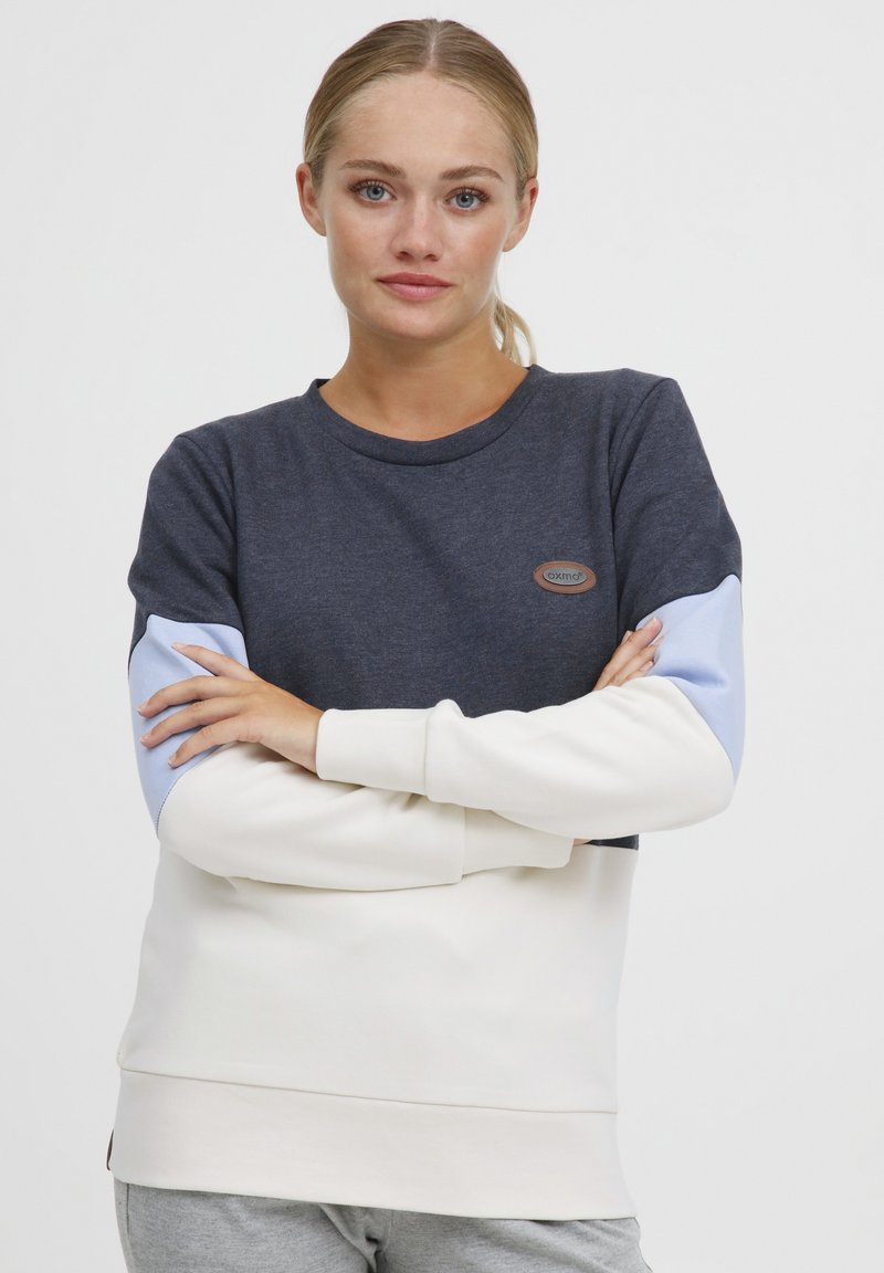 Sweatshirt avec un corps bleu marine foncé, des manches bleu clair et un bas crème. Mélange de coton avec un col rond et un patch logo.