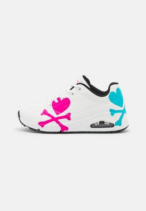 Witte sneaker met zwarte zool en gevoerde kraag, met groot roze hart en gekruiste beenderen aan de zijkant en blauw hart en gekruiste beenderen op de hiel.