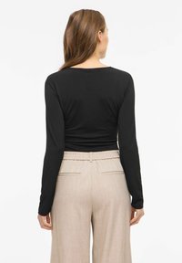 Must pikkade varrukatega särk ja beežid lahtised püksid, millel on lõdvaistme vöökoht ja küljetaskud. Sile ja veniv materjal.