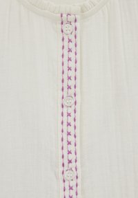 Bílá látková halenka s centrálním plaketem se třemi knoflíky a fialovým vyšíváním podél řady knoflíků. Vráskavá textura.