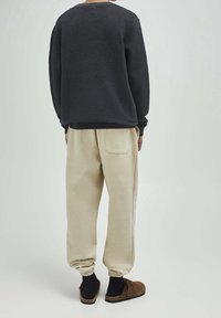 Ciemny sweter o fakturowanej powierzchni i beżowe, zwężane spodnie dresowe z elastycznym mankietem, kieszeniami oraz brązowymi butami wsuwanymi.