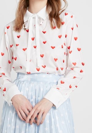 Witte blouse met rode hartpatronen, voorzien van een kraag en strik, gecombineerd met een lichtblauwe geplooide rok met stermotieven.