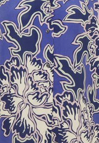 Short-sleeve shirt in a blue fabric featuring large white floral patterns outlined in purple and green, with black buttons at the front.