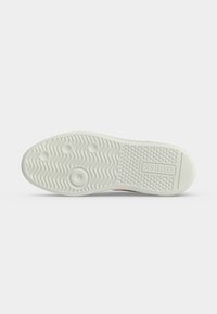 Semelle en caoutchouc blanche avec une semelle extérieure texturée, motifs circulaires et ondulés, et logo "GUESS" embossé près du talon.
