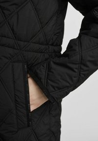 Czarna pikowana kurtka z diagonalnym przeszyciem, zapinaną na zamek kieszenią oraz fakturowanym wykończeniem z logo na obrzeżu.