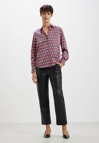 Camicia multicolore con sfondo rosa e un motivo geometrico a quadrati verdi e neri; abbinata a pantaloni in pelle nera lucida.