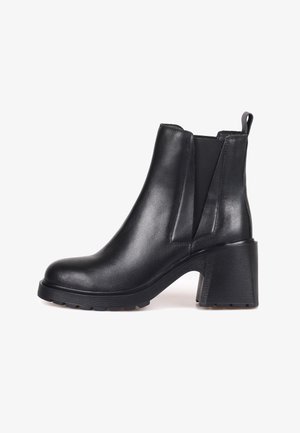 Bota de tobillo de cuero negra con un tacón grueso, paneles laterales elásticos y una suela de goma texturizada. Presenta un acabado suave y una puntera redondeada.