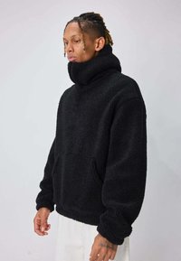 Polaire noire à col montant, coupe surdimensionnée, avec poche avant. Texture douce et poignets élastiques, idéale pour un look décontracté.