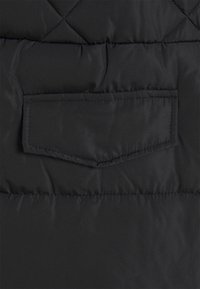 Tissu de veste matelassée noire avec une poche à rabat horizontale présentant des coutures détaillées.
