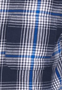 Camicia a scacchi nei colori blu navy, bianco e blu. Tessuto morbido con una stampa a rete e una tasca petto singola. Fit regolare.