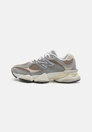 Grey and beige New Balance sneaker with white laces, mesh and suede panels, and a chunky white and black sole, shown in profile.